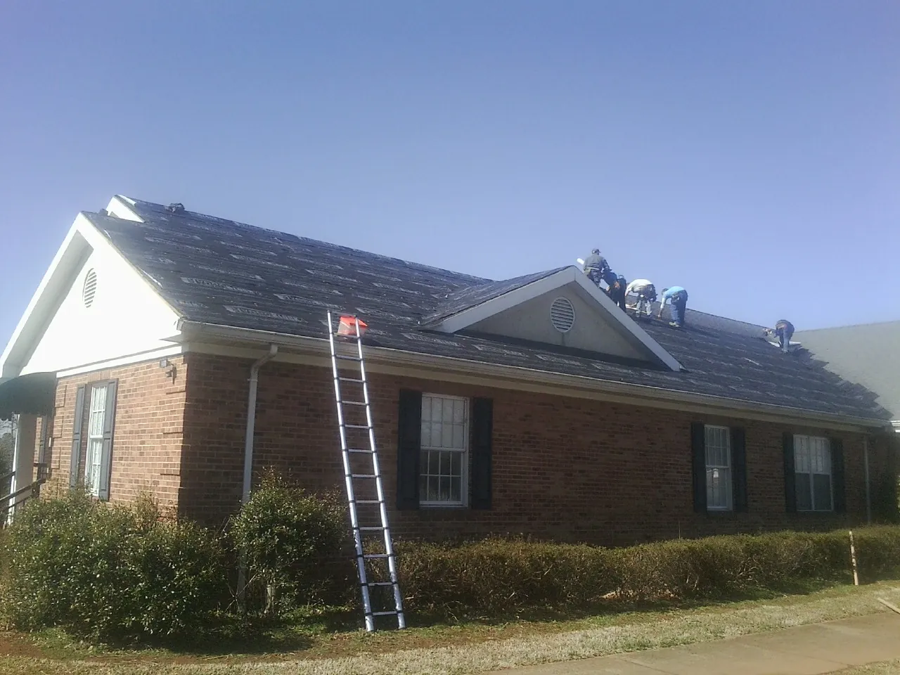 Crew tearing shingles off a brick ranch roof with a ladder set — Emergency Roof Repair work by our crew in Hooksett