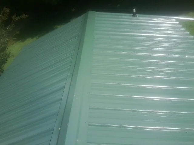 New green metal panels meeting at the ridge of a roof — Flat Roof Repair work by our crew in Hooksett