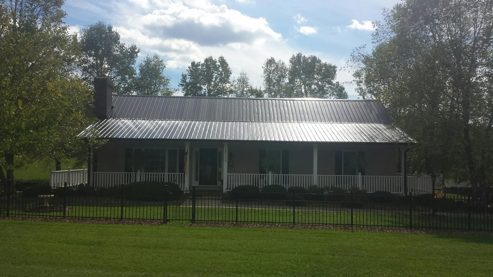 Gray metal roof on a brick ranch with a full width front porch — Gutter Guard Installation work by our crew in Hooksett